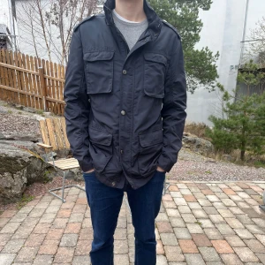 Marinblå Hackett field-jacket - Snygg marinblå Hackett jacka med flera fickor och knappar framtill. Perfekt för en stilren look.