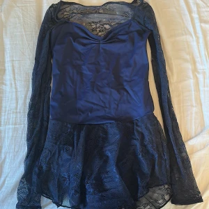 Marinblå spetsklänning - Snygg marinblå klänning med spetsdetaljer och långärmad design. Klänningen har en elegant v-ringning och en kort längd som passar perfekt för festliga tillfällen.