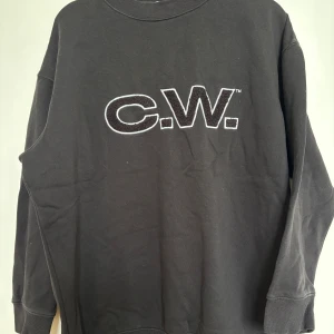 Svart sweatshirt från Carin Wester - Säljer en svart sweatshirt från Carin Wester med C.W. tryck på framsidan i storlek XS men skulle säga att den sitter mer som en M/L. Färgen är mörkare i verkligheten.