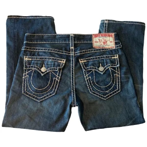 Blå jeans från True Religion - Snygga Trueys med vita sömmar och ikoniska bakfickor med lock och knappar. (OBS! Byxan har ett hål vid vänster knäskål, mer bilder kan skickas privat) Jeansen är insydda nere vid hälen för att ge den lite mindre benöppning (26cm). Måtten är 38x32, mått: midja:52cm innerben:73cm ytterben:103cm. Säljer de eftersom de inte riktigt är min stil längre.