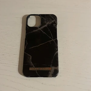 Svart marmorerat mobilskal från iDeal of Sweden IPhone 12/13 - Snyggt svart mobilskal med marmorerat mönster från iDeal of Sweden. Skalet har en elegant design med en metallisk logotypdetalj. Perfekt för att ge din telefon ett stilrent utseende. iPhone 12/13. Ny pris: 299 kr