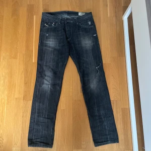 Svarta jeans från Diesel - Snygga mörkblå jeans från Diesel med en cool slitningseffekt. De har en klassisk femficksdesign och knappgylf. Två missfärgningar förekommer se bild 3 och 4. Ser dock snyggt ut med slitningarna. 