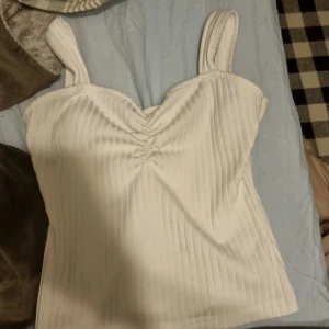Vit ribbad linnetopp från Shein - Säljer en stilren vit ribbad linnetopp från Shein. Toppen har breda axelband och en snygg rynkdetalj framtill som ger en fin form. Perfekt för varma dagar eller som ett lager under en jacka.