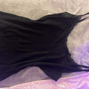 Svart linne med spetsdetaljer - Säljer ett stilrent svart linne med spetsdetaljer längs kanterna. Perfekt för en elegant look