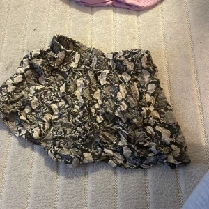 Mönstrad kjol med volanger - Säljer en cool kjol med ett unikt mönster i jordnära toner. Kjolen har volanger som ger en extra touch och en elastisk midja för bekväm passform. Perfekt för att sticka ut i mängden!