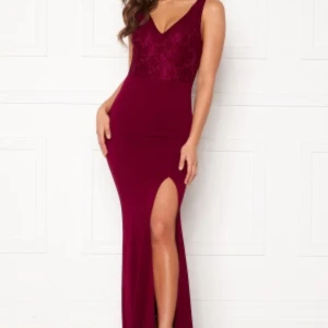 Vinröd långklänning från Bubbleroom - Elegant vinröd långklänning från Bubbleroom med spetsdetaljer och v-ringning. Klänningen har en slits och dragkedja i sidan för en smickrande passform. Perfekt för speciella tillfällen. Använd vid endast ett tillfälle 