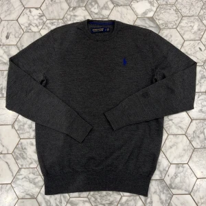 Grå tröja från Polo Golf Ralph Lauren - Säljer en stilren grå tröja från Polo Golf Ralph Lauren. Tröjan har en diskret blå logga på bröstet och är tillverkad i ett mjukt merinoull material. Perfekt för en avslappnad och elegant look. Den  har en diskret lagning bredvid loggan men det är inget man lägger märke till. Skriv gärna vid frågor, priset är inte hugget i sten!