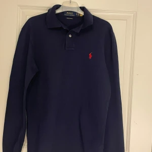 Mörkblå long sleeve piké - Polo Ralph Lauren - Säljer en långärmad piké från Careofcarl. Nypriset:1499. Tröjan är bara använd ett fåtal gånger, där med är skicket perfekt, utan slitningar eller liknande!