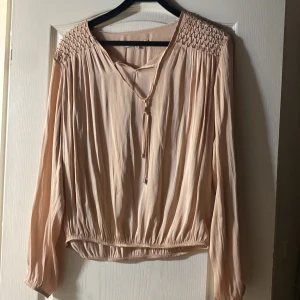 Bronz beige blus  -  Väldigt tunn och Skön Blus med silvriga detaljer på axlarna. Den har lite fläckar på magen som går att få bort annars är den väldigt fin