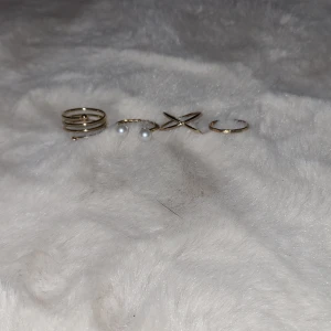 Set med guldiga ringar - Säljer ett set med stilrena guldiga ringar. Setet innehåller en ring med tre band, en med två pärlor, en korsad design och en enkel slät ring. Perfekt för att mixa och matcha!