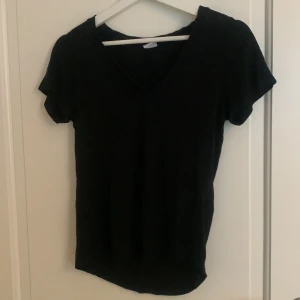 Svart v-ringad t-shirt - Säljer en stilren svart t-shirt med v-ringning. Perfekt basplagg för alla tillfällen. Den har korta ärmar och är gjord i ett mjukt material. Snören som går från axlarna till mitten av v-ringningen. 