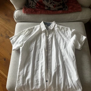 Vit linneskjorta från Springfield - Säljer en stilren vit skjorta från Springfield's Linen Collection. Skjortan har korta ärmar och en klassisk krage med ett snyggt mönster på insidan. Perfekt för varma dagar med sin luftiga passform.