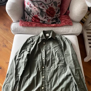 Grön skjorta från H&M - Snygg grön skjorta från H&M med klassisk krage och knappar framtill. Skjortan har en bröstficka och långa ärmar, perfekt för en stilren look. Tillverkad i ett bekvämt material som passar bra till olika tillfällen.