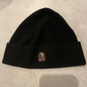 Svart mössa från Parajumpers - Snygg svart mössa från Parajumpers med ribbad kant och ett broderat märke framtill. Perfekt för kyliga dagar och en stilren look.