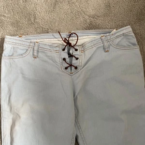 Ljusblå jeans med snörning - Snygga ljusblå jeans med unik snörning framtill. De har en klassisk femficksdesign och en bootcut-stil som ger en retro känsla. Perfekta för en avslappnad look med en twist.