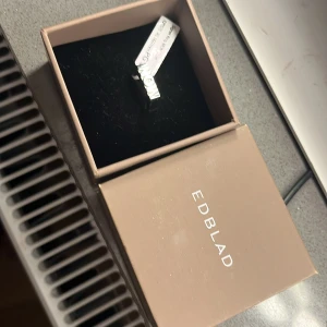 Silverfärgat halsband från Edblad - Elegant silverfärgat halsband från Edblad med ett hängsmycke i form av ordet 'MOM'. Perfekt som en personlig present eller för att bära själv. Kommer i en stilren förpackning.Aldrig använd glömde byta den i stolek 16.0