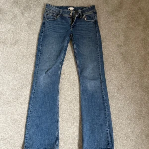 Blå jeans från Gina Tricot - Snygga blå jeans från Gina Tricot i en klassisk bootcut-stil. De har en låg midja och är utrustade med knappar framtill. Perfekta för en avslappnad look.