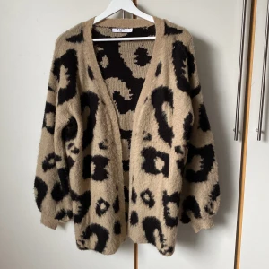 Beige leopardmönstrad kofta från NA-KD - En supermjuk och beige kofta från NA-KD med svart leopardmönster. Koftan är öppen utan knäppning och långa ärmar med ribbade muddar. Längd 80 cm. Storlek XS men funkar bra på mig som har 40/42.  Perfekt för att lägga till lite edge till din outfit! 🐆