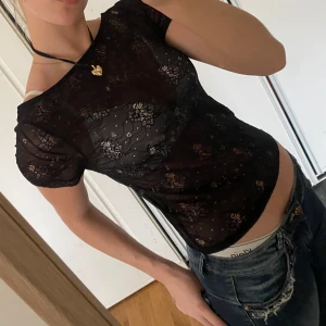 Svart spetsblus - Snygg svart spetsblus med korta ärmar och ett transparent mönster. Blusen har en tight passform och är idealisk för en kväll ute.