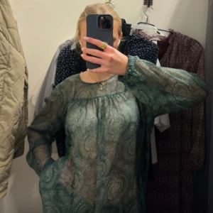 Grön mönstrad blus - Säljer en elegant grön blus med ett subtilt mönster. Blusen har långa ärmar och en luftig passform, perfekt för en stilren look. Passar bra till både jeans och kjol.