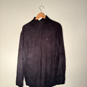 Retro Nike fleece half zip - Svart half zip fleece från Nike. Enkel design med en liten Nike-logga på bröstet. Perfekt för kyliga dagar och ger en sportig look. ”Gummit” på dragkedjan har försvunnit men inget som påverkar mer än att det är lite mindre att ta i när man ska knäppa.