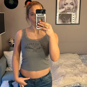 Grå ribbad linnetopp med spetsdetaljer - Säljer en grå ribbad linnetopp med spetsdetaljer runt halsringningen. Toppen har ett tryck framtill och är i storlek S!