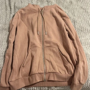 Beige huvtröja med dragkedja - Säljer en beige huvtröja med dragkedja och fickor framtill. Tröjan har långa ärmar och en justerbar huva med snören. Perfekt för en avslappnad stil. Har väldigt små fläckar vid luvan. Storlek M. 60% Bomull, 40% Polyester