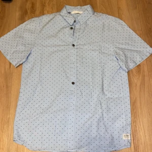 Ljusblå kortärmad skjorta från Columbia - Säljer en ljusblå kortärmad skjorta från Columbia med små prickar. Skjortan har knappar framtill och en klassisk krage. Perfekt för varma dagar!