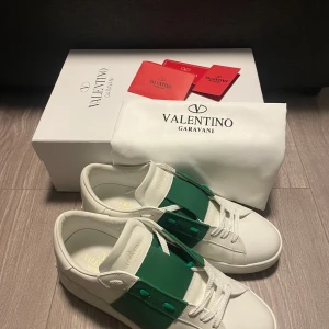 Valentino skor - Snygga vita valentino garavani open sneakers i kalvskinn med en grön rem över snörningen. Storlek 43 och är i väldigt fint skick. Endast använda några gånger då skorna var för stora för mig. Allt är i perfekt skick förutom en liten skada i lådan, kontakta med fler frågor!