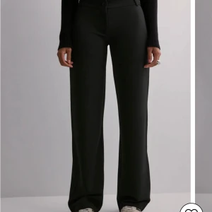 Svarta kostymbyxor - Eleganta svarta kostymbyxor med hög midja och rak passform. Byxorna har en klassisk design med knappar och dragkedja framtill. Perfekta för en stilren look.
