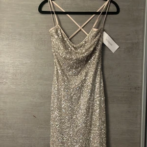 Glittrig balklänning med öppen rygg - Säljer balklänning den är aldrig använd (prislapp är kvar). Snygg glittrig guldklänning med smala axelband och öppen rygg. Klänningen är öppen i ryggen och har en perfekt passform. 
