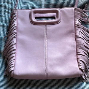 Rosa axelväska med fransar från Maje - Säljer en snygg rosa axelväska från Maje med coola fransdetaljer på sidorna. Väskan har ett praktiskt handtag och en justerbar axelrem. Perfekt för att ge din outfit en extra touch!den är inte använd så mycket har tagit hand om den riktigt bra🥰