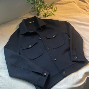 Marinblå overshirt  - Säljer en stilren mörkblå overshirt från Zara. Den har långa ärmar och knappar framtill samt två bröstfickor med knappar. Perfekt för lager-på-lager-stil. nyskick, bara använd ett par gånger Mått: Axelbredd: 49cm Längd: 63 Tveka inte på att skriva om du har några funderingar!