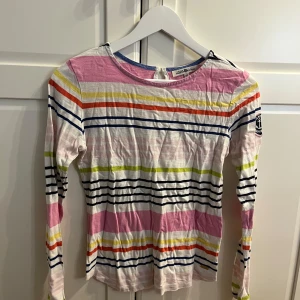 Randig långärmad tröja från Hampton Republic - Säljer en färgglad randig tröja från Hampton Republic. Tröjan har långa ärmar och ett märke på ärmen. Den är i flera färger som rosa, blå, gul och vit. Perfekt för en avslappnad stil.