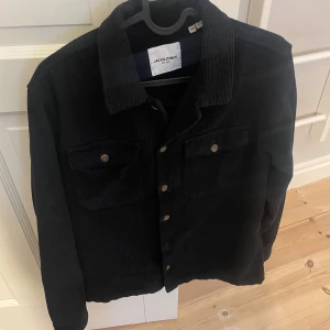 Svart manchesterjacka från Jack & Jones - Säljer en snygg svart manchesterjacka från Jack & Jones. Jackan har långa ärmar och knappar framtill. Perfekt för en stilren look. Två bröstfickor med knappar ger extra stil och funktion. 