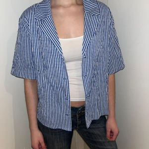 Blå och vit rutig skjorta från Monki - Säljer en blå och vit rutig skjorta från Monki. Skjortan har korta ärmar och knappar framtill. Perfekt för en avslappnad stil med en klassisk touch. Knappt använd!!