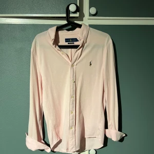 Ljusrosa skjorta från Ralph Lauren - Säljer en stilren ljusrosa skjorta från Ralph Lauren. Skjortan har långa ärmar och är broderad med den klassiska logotypen på bröstet. Perfekt för en elegant look!
