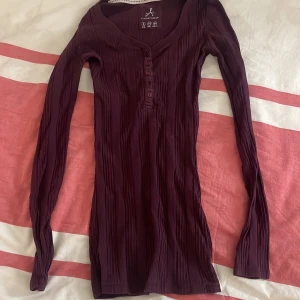 Vinröd ribbad tröja från Atmosphere - Säljer en tajt vinröd ribbad tröja från Atmosphere med knappar framtill. Tröjan har en v-ringad design och långa ärmar, perfekt för kyligare dagar. Passar bra till både jeans och kjol. Hör av dig vid intresse! 💜