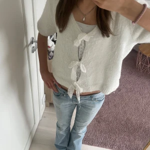 Vit kofta med knytband - Säljer en söt vit kofta med korta ärmar och knytband framtill. Perfekt för en avslappnad stil. Koftan har en mjuk och bekväm passform. Den är lite nopprig 