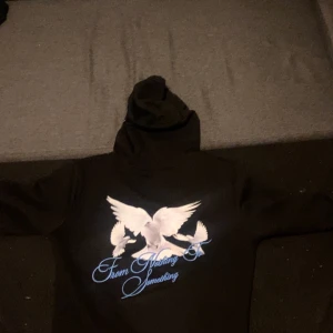 Svart hoodie från Hoodrich - Säljer en svart hoodie från Hoodrich med tryck av vita duvor och texten 'From Nothing to Something'. Hoodien har en klassisk design med dragsko i huvan och långa ärmar. Perfekt för en avslappnad stil.