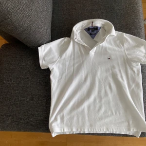 Vit pikétröja från Tommy Hilfiger - Säljer en stilren vit pikétröja från Tommy Hilfiger i storlek S. Tröjan är tillverkad i 100% bomull och har en klassisk krage med korta ärmar. Perfekt för en avslappnad och snygg look. 🕶️