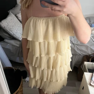 Ljusgul volangklänning - Säljer en ljusgul klänning med flera lager av volanger. Klänningen är ärmlös och har en kort längd. Går att ha med band eller utan. 