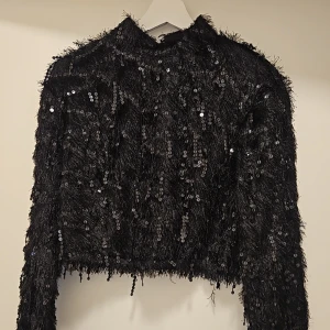 Svart paljettprydd tröja - Säljer en svart tröja med paljetter som ger en glittrig look. Tröjan har långa ärmar och en croppad design, perfekt för en festlig kväll. Den är både stilren och iögonfallande. Storlek S i mycket gott skick! 