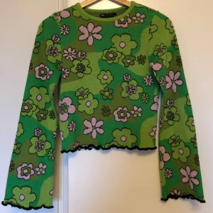 Grön blommig stickad tröja från ASOS - grön stickad tröja från ASOS med  blommönster. Slutar i midjehöjd, har utsvängda ärmar och har en vågig kant i svart. Storlek 32 men passar mig som är 34