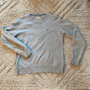 Grå tröja från GANT - Säljer en stilren grå tröja från GANT med rund halsringning och ett diskret broderat emblem på bröstet. Tröjan har långa ärmar och är perfekt för en avslappnad look. Passar bra till både jeans och chinos. Perfekt för kyligare dagar! Hör av dig vid frågor!