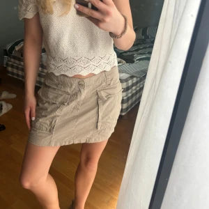 Beige kortkjol med fickor - Säljer en beige kortkjol med två stora fickor framtill och knappstängning. Kjolen har en avslappnad passform och är perfekt för dig som gillar en enkel men ändå snygg stil. Passar till både sneakers och sandaler. Materialet känns lätt och skönt mot huden.