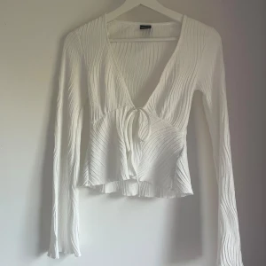 Vit omlottopp från Gina Tricot 🤍 - Supersnygg vit omlottopp från Gina Tricot i storlek XS. Toppen har lång ärm, v-ringning och knyt framtill. Materialet är ribbat med vågiga strukturer som ger en cool look. Perfekt att styla med jeans eller kjol för en trendig outfit. Pris kan diskuteras.
