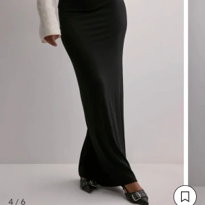 Svart långkjol i stretchigt tyg - Supersnygg svart långkjol med tight passform och mjukt, stretchigt material som följer kroppen. Perfekt att styla med en stickad tröja eller crop top för en clean och trendig look.