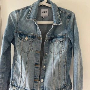 Ljusblå jeansjacka från Zara, S - Snygg ljusblå jeansjacka från Zara i klassisk modell med silverfärgade knappar och två bröstfickor. Jackan har en rak passform, krage och slitna detaljer vid fållen för en cool vibe. Perfekt att slänga över en hoodie eller t-shirt. Jackan är i ny skick. 