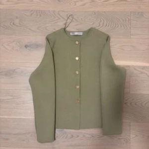Olivgrön cardigan med knappar - Snygg olivgrön cardigan med raka linjer och guldiga knappar framtill. lång ärm och är tillverkad i ett stickat material som känns både mjukt och stilrent. Perfekt för dig som gillar minimalistisk och clean stil.